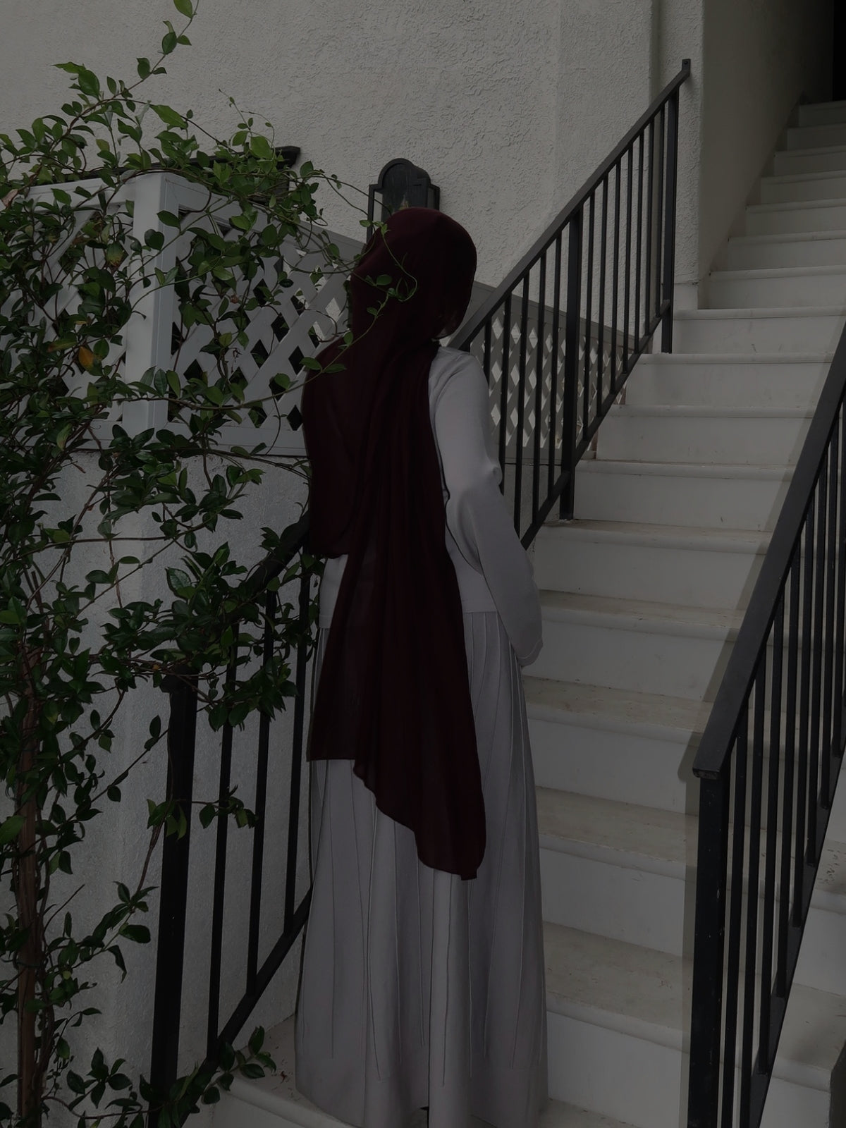 Woman in a burgundy modal hijab and white maxi dress walking up an outdoor staircase